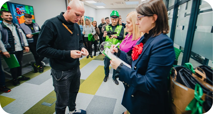 Dwoje pracowników w odzieży ochronnej rozmawia wewnątrz hali logistycznej.