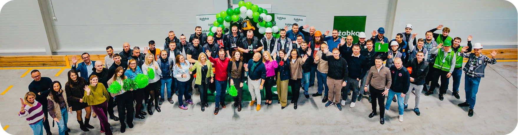 Pamiątkowe zdjęcie grupowe kilkudziesięciu pracowników logistyki przed budynkiem firmy.