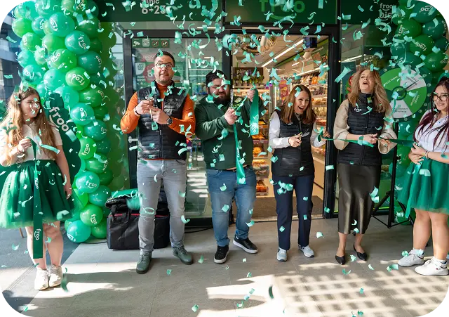Grupa pracowników świętująca event firmowy na tle ściany z zielonych balonów.