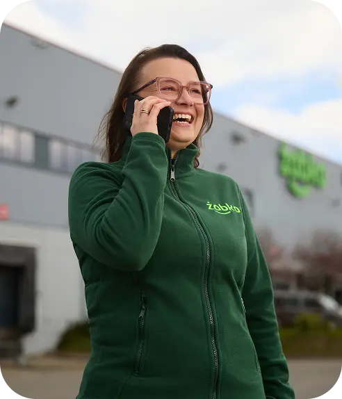 Uśmiechnięta kobieta w zielonej kurtce rozmawiająca przez telefon na świeżym powietrzu.